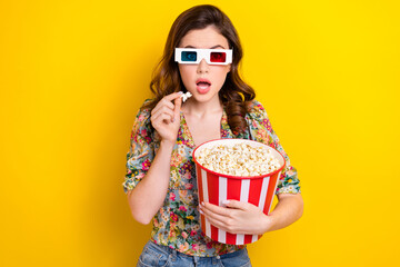 Portrait of impressed girl hand hold pop corn bucket open mouth watch movie 3d glasses isolated on yellow color background