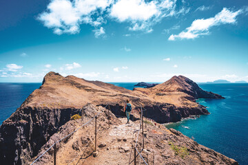 Wall Mural - Athletic woman hikes along hike trail with scenic view on the beautiful foothills of the Madeiran island. São Lourenço, Madeira Island, Portugal, Europe.