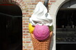 Überlebensgroße Eistüte mit Eiskugel und Sahne vor einer Eisdiele und Gelateria als Teil des Unesco Weltkulturerbe im Sonnenschein in den Gassen der Altstadt von Brügge in Westflandern in Belgien