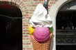 Überlebensgroße Eistüte mit Eiskugel und Sahne vor einer Eisdiele und Gelateria als Teil des Unesco Weltkulturerbe im Sonnenschein in den Gassen der Altstadt von Brügge in Westflandern in Belgien