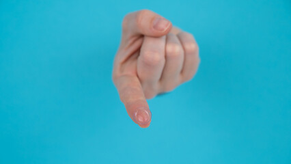 Wall Mural - A woman's hand sticks out through a blue paper background and holds a contact lens.