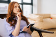 © dikushin - Close-up face of thoughtful young woman sitting on comfy chair at home and thinking about something with pen in mouth and notebook on hand. Pensive female try find solution, writing diary.