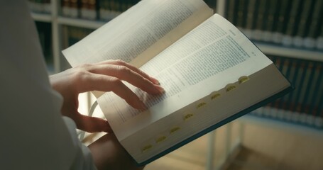 Close-up female hands holding and reading a book in public library. Theologian studies the history of the World.