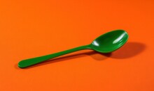  A Green Plastic Spoon On An Orange Background With A Shadow.  Generative Ai
