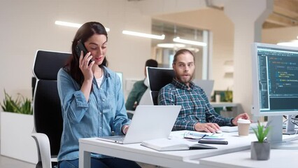 Wall Mural - two caucasian programmers sitting in front of computers. pretty woman talking loudly on phone and di