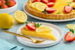 A piece of lemon tart decorated with strawberries, mint and a slice of citrus on a white plate. French classic dessert. Selective focus