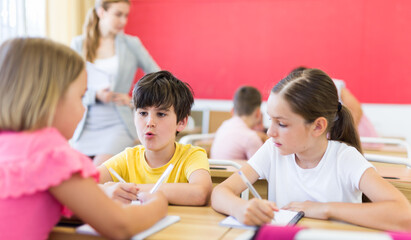 Wall Mural - Schoolkids performing group tasks during lesson. Their teacher standing and observing.