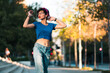 © Nano - bella mujer adolescente estilo 80s 90s andando en skate en la ciudad, con maquillaje, anteojos y jeans. en un día soleado al atardecer.