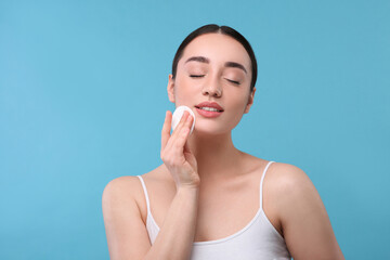 Wall Mural - Beautiful woman removing makeup with cotton pad on light blue background