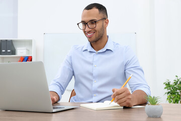 Canvas Print - Happy young intern working with laptop at table in modern office