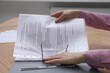 © New Africa - Woman putting punched pocket with document into folder at wooden table, closeup
