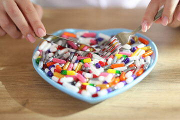 Wall Mural - Female hands holding fork and knife and pills in heart-shaped bowl