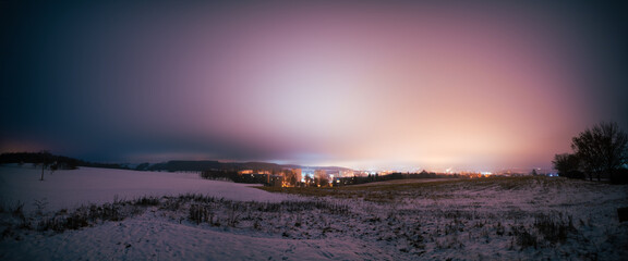 Poster - night landscape of a snowy field and a city  with lights on the horizon