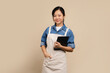 © PBXStudio - Close up happy young asian woman business owner wear apron and holding tablet isolated on brown background for SME franchise investment concept