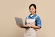 © PBXStudio - smiling young Asian woman barista barman employee wearing brown apron work in coffee shop using work on laptop pc computer on light brown background. Small business startup concept