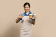 © PBXStudio - Coffee shop, small business and startup concept. Cheerful asian female barista wear cream color apron, She pointed to the brown coffee cup in her hand.