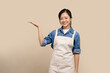 © PBXStudio - Young asian woman waiter in apron with advertises copy space on light brown isolated background