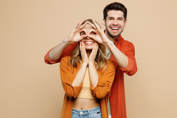 Wall Mural - Young fun couple two friends family man woman wear casual clothes looking camera hold hands fingers near eyes pov glasses gesture together isolated on pastel plain light beige color background studio.