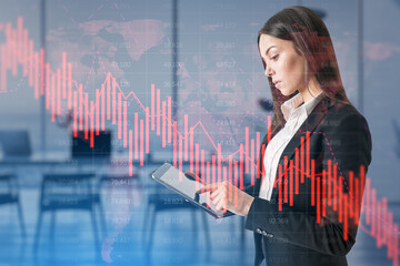 Canvas Print - Attractive thoughtful european businesswoman using tablet with falling red business graph grid on blurry office interior background. Crisis, recession and stock market concept. Double exposure.