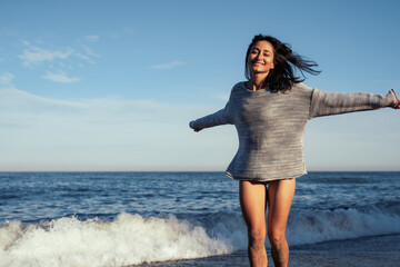 young beautiful brunette girl walks on the sand on the seashore in a swimsuit and a sweater