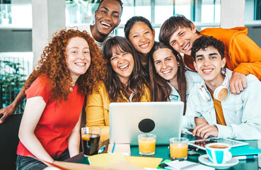 Multiracial university students sitting together at table with books and laptop - Happy young people doing group study in high school library - Life style concept with guys and girls in college campus