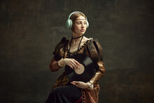 Portrait Of Pretty Young Girl, Royal Person In Elegant Vintage Dress Listening To Music In Headphones, Holding Vinyl On Dark Green Background. Concept Of History, Renaissance Art, Comparison Of Eras