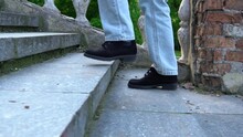 Woman Legs In Jeans Walking On Ancient Stair Side View. Female Foot In Black Suede Shoe Go Up Step By Step On Old Classic Balustrade. Feet Coming And Climbing Up. Disrupted Stairway And Stone Railings