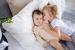 © Any Grant - older sister baby kisses and hugs baby at home on the bed, love and friendship of sisters in the family