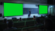 © Gorodenkoff - Young Male Teacher Giving a Lecture, Showing Slides on a Green Screen Mock Up Display to a Diverse Multiethnic Group of Female and Male Students in Dark College Auditorium