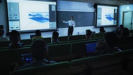 Fototapete - Young Female Teacher Giving an Architectural Engineering Lecture to Diverse Multiethnic Group of Women and Male Students in Dark College Room. Projecting Slideshow with a Private House Blueprint