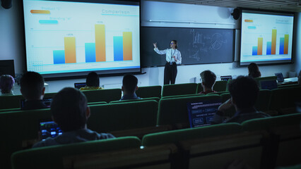 Leinwandbilder - Young University Professor Explaining the Importance of Branding and Marketing Campaigns to a Group of Diverse Multiethnic Students in a Dark Auditorium. Female Teacher Showing Business Charts Data