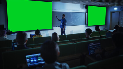Aufkleber - Young University Professor Explaining a Lecture, Pointing on a Green Screen Mock Up Display. Group of Diverse Multiethnic Students Study in a Dark Auditorium. Teacher Showing Content on Big Screens