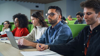 Fototapete - Smart Handsome Male Student Studying in University with Diverse Multiethnic Classmates. Young Man is Using a Laptop Computer to Summarize the Lecture, Study at Home and Pass the Exams