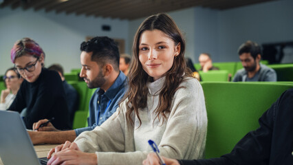 Fototapete - Beautiful Smart Female Student Studying in University with Diverse Multiethnic Classmates. Portrait of a Happy Caucasian Female Looking at Camera and Smiling. She is Using a Laptop Computer