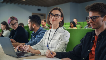 Leinwandbilder - Portrait of a Happy Young Caucasian Female in Glasses Looking at Camera and Smiling. Young Female Student Using Laptop Computer and Studying in University with Diverse Multiethnic Classmates