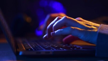 Close-up image of human hands typing on laptop keyboard, working online at home office with neon lights. Business, remote work, programming, journalism, gaming, modern technologies, freelance concept