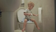 Baby Toddler Sitting On Toilet Learning To Clean His Hygiene Bottom Butt Anus Toilet Paper. Potty Training Child In Bathroom. Little Boy Kid Pulls Toilet Paper Sweep His Back After Poop Poo Defecate
