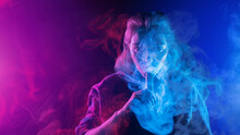 Woman Smokes Vape. Girl Releases Steam From Device For Vaping. Lady Vaper. Woman With Electronic Cigarettes. Vaper On Neon Background. Vape Pen For Smoking Vapor. Hobby Vaping. Vape Smoker