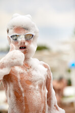 Happy Little Boy With Goggles And Foam On His Head Having Fun In A Water Park, In Wet Swimwear At A Foam Party Or Holiday On A Sunny Hot Summer Day