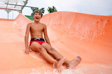 Wall Mural - A little boy slides down an orange water slide in the water park, a child's cheerful mood, holidays