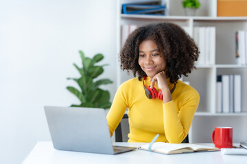 Young woman using laptop to work from home. Female student with curly hair sitting and working with laptop in university