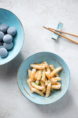 Wall Mural - Turquoise bowls with korean traditional tteokbokki and mochi, vertical shot on a light-beige stone background, high angle view