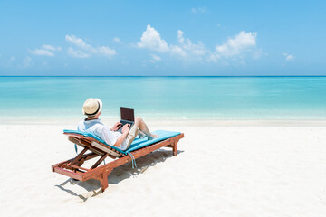Wall Mural - young man working as digital nomad on the beach with a laptop
