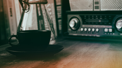 Wall Mural - coffee brewing jug, vintage radio, a black coffee cup and saucer on a brown wooden table, with books in the background, vintage caffee wallpaper