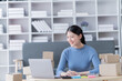 © Tj - Asian business woman siting on sofa using a laptop and notebook checking order online shipping boxes at home. Starting SME Small business entrepreneur freelance. Online business, SME Work