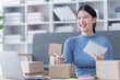 © Tj - Asian business woman siting on sofa using a laptop and notebook checking order online shipping boxes at home. Starting SME Small business entrepreneur freelance. Online business, SME Work