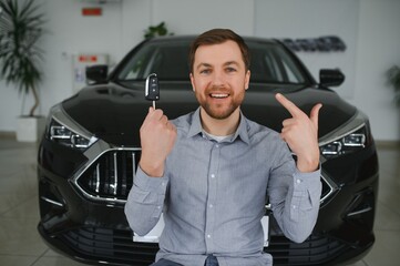 Wall Mural - Emotional handsome guy raising hand up and smiling at camera. Rich man buying auto at luxury dealership salon