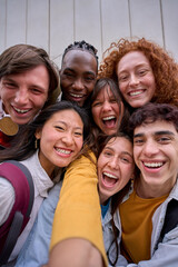 Wall Mural - Vertical cell phone selfie of excited multiracial group of erasmus college students together outside. Cheerful smiling young friends pose laughing for photo. Happy people on campus.