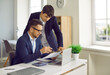 © Studio Romantic - Male financial director giving directions to his assistant while working on financial report. Man in suit is sitting at laptop, holding paper document and explaining something to his colleague.