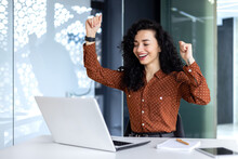 Young Hispanic Business Woman Got Good Work Result, Business Woman Is Happy And Celebrating Victory Holding Hands Up Looking And Reading From Laptop Screen.